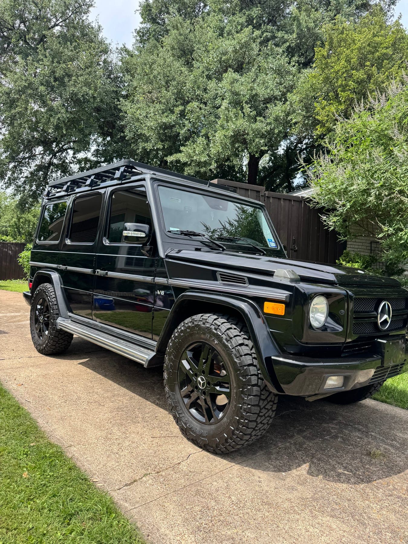 A detailed black Mercedes-Benz G-Class, front three-quarter view in a driveway
